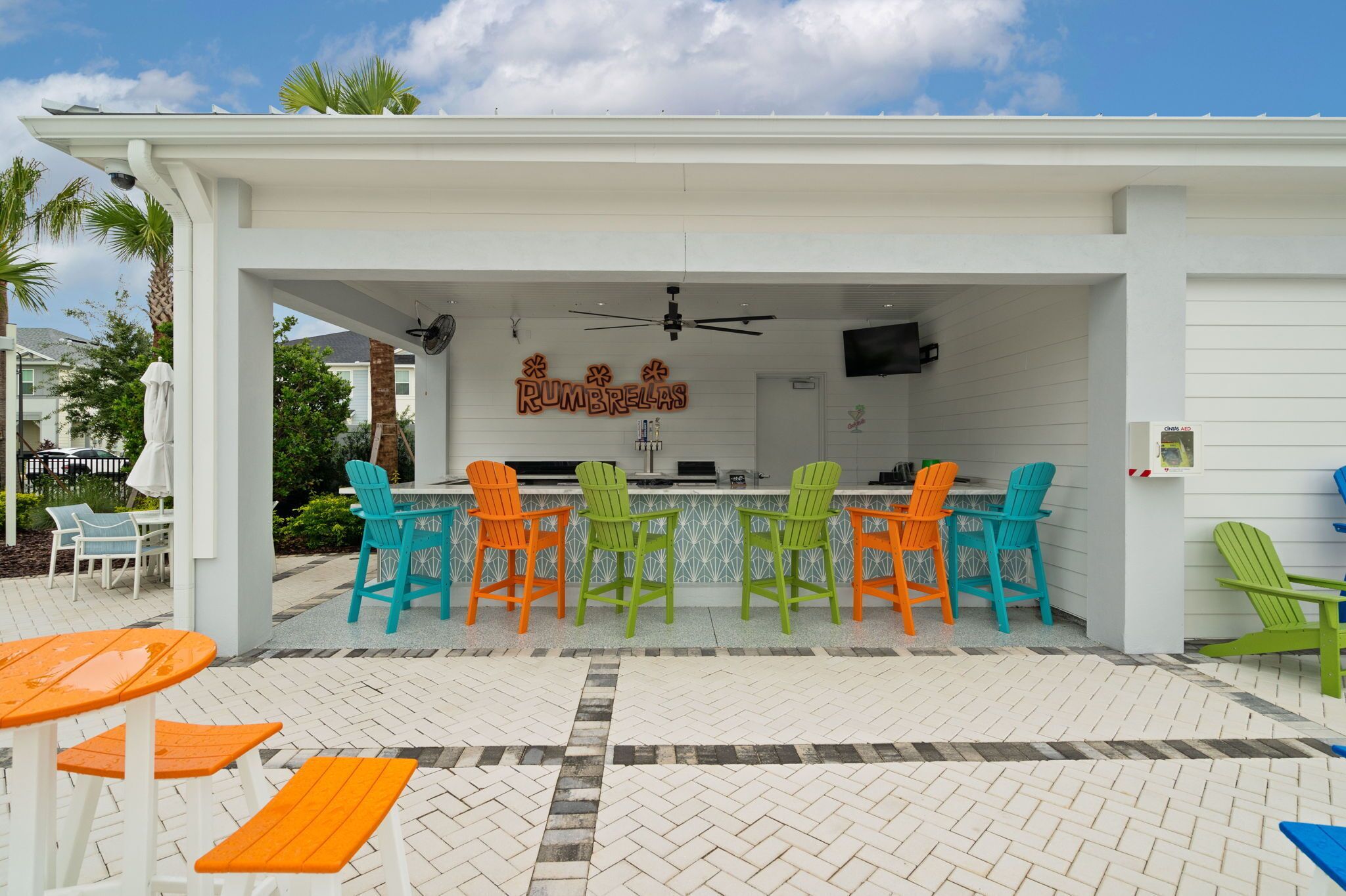 Une terrasse extérieure dotée d’un espace salon couvert, d’un bar et d’une enseigne sur laquelle on peut lire « RUMBRELLAS ».