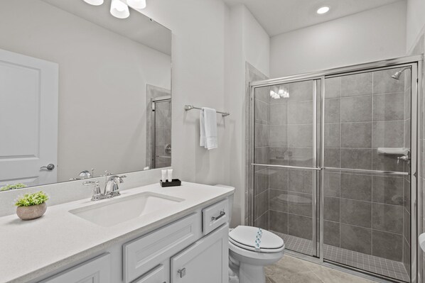 Une salle de bain moderne avec un grand miroir, un lavabo blanc et une douche à parois de verre.