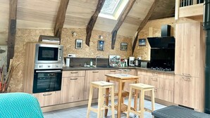 A rustic kitchen with wooden beams, a skylight, a stove, a microwave, and a sink.