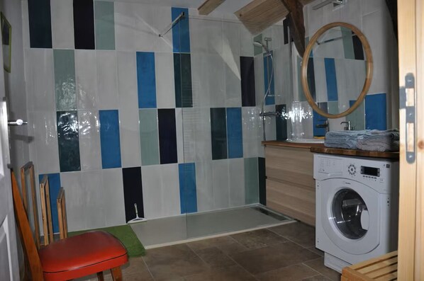 A small, compact bathroom with a shower, a washing machine, and a mirror.