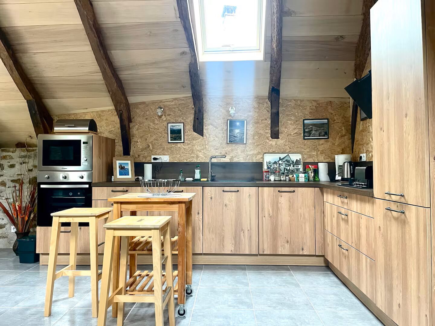 Une cuisine avec des meubles de rangement en bois, un four encastré et un petit coin repas équipé de tabourets.