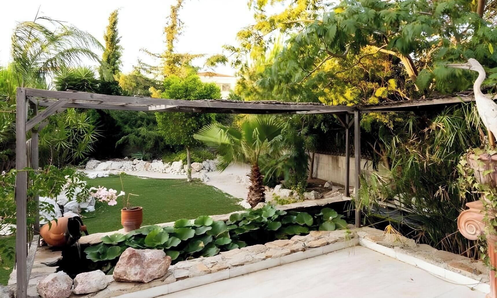 Un jardin agrémenté d’une pergola en bois, d’un petit étang et de diverses plantes.
