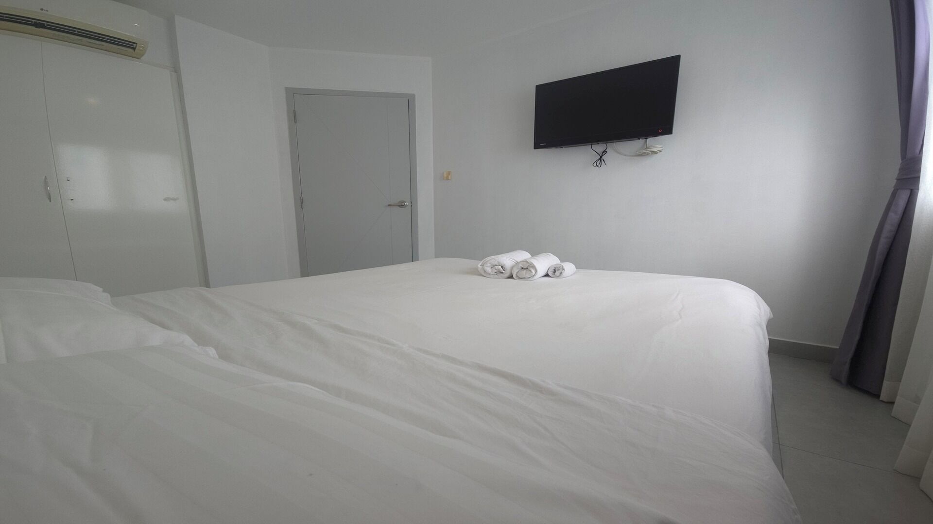 Una habitación de hotel con una cama, un televisor de pantalla plana en la pared y una puerta.