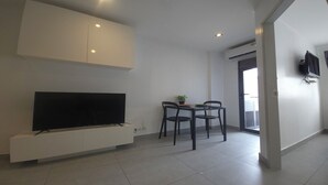 Een moderne woonkamer met een flatscreen televisie, een eethoek met twee stoelen en een kleine tafel, en een witte kast boven de televisie.