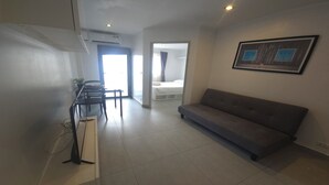 Een moderne woonkamer met een grijze bank, een eethoek met stoelen en een tafel, en een slaapkamer met een bed en gordijnen.