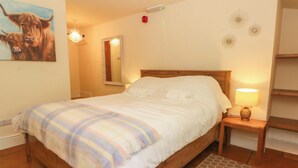 A bedroom with a wooden bed, a bedside lamp, a mirror, and a painting of bulls on the wall. - The Old Shippon (Macclesfield)