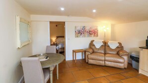 A cozy living room with a dining table, a leather sofa, and a painting on the wall. - The Old Shippon (Macclesfield)
