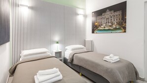 Ein Hotelzimmer mit zwei Betten, einem Nachttisch, einer Lampe und einem Bilderrahmen mit einem Gebäude darauf.