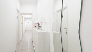 Ein Flur mit weißen Wänden, einem gefliesten Boden, einem weißen Schrank mit Spiegel und einer Tür am Ende.
