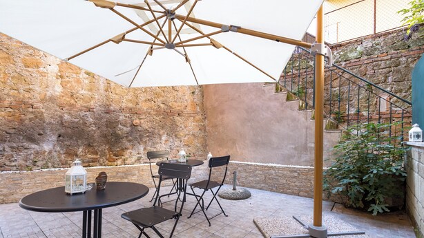 Eine Terrasse im Freien mit einem runden Tisch und Stühlen, einem hängenden Sonnenschirm und einer Treppe, die zu einer erhöhten Ebene führt.