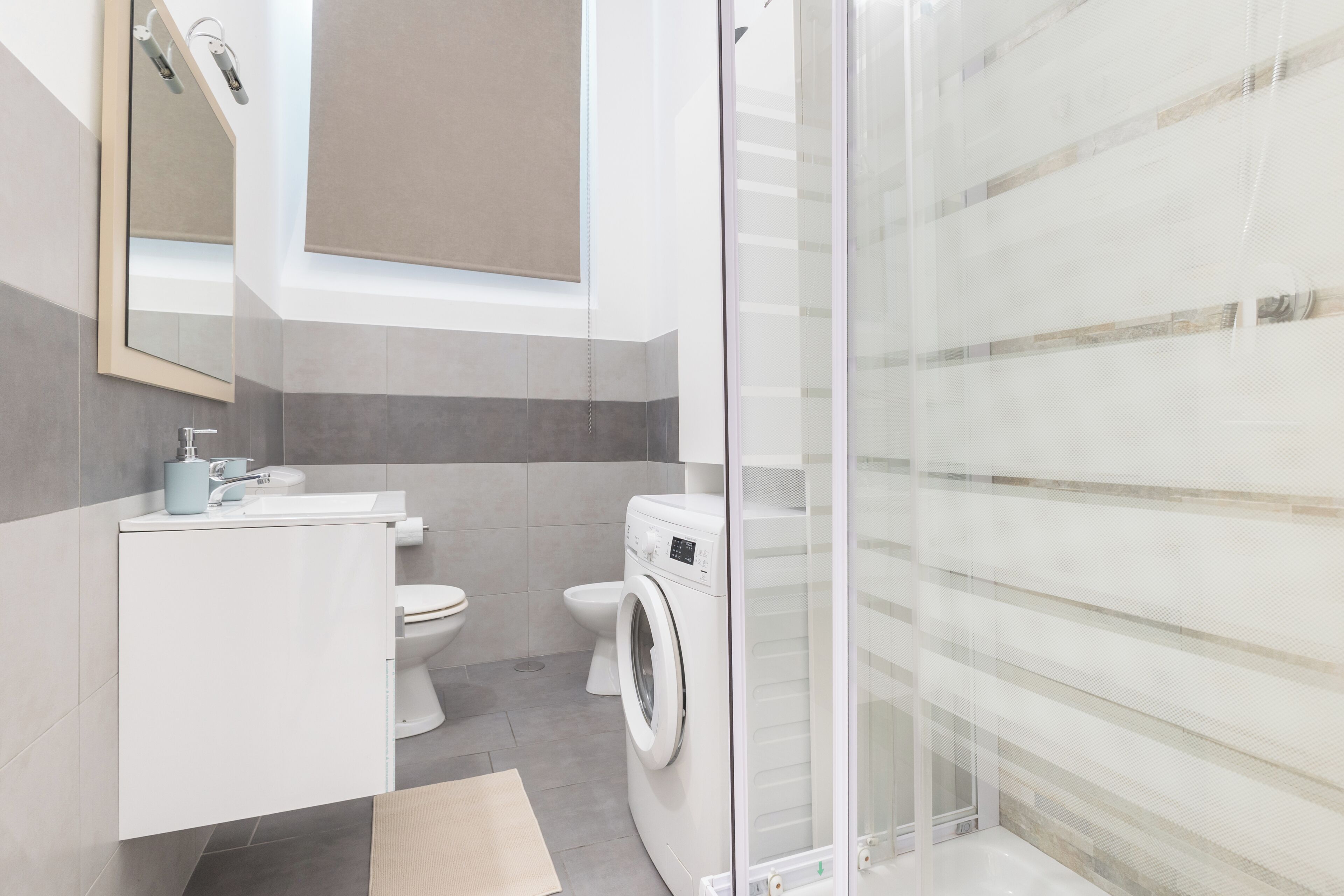 Une salle de bain moderne dotée d’une douche à parois de verre, d’un lave-linge encastré et de toilettes.