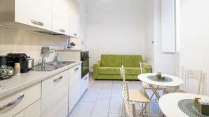 Eine kleine Küche mit Spüle, Herd und einem grünen Sofa im Hintergrund.