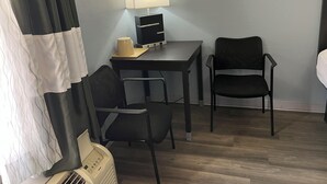 A hotel room with a desk, two chairs, a lamp, and a heater. - Old Town Inn - St Augustine South (Elkton)