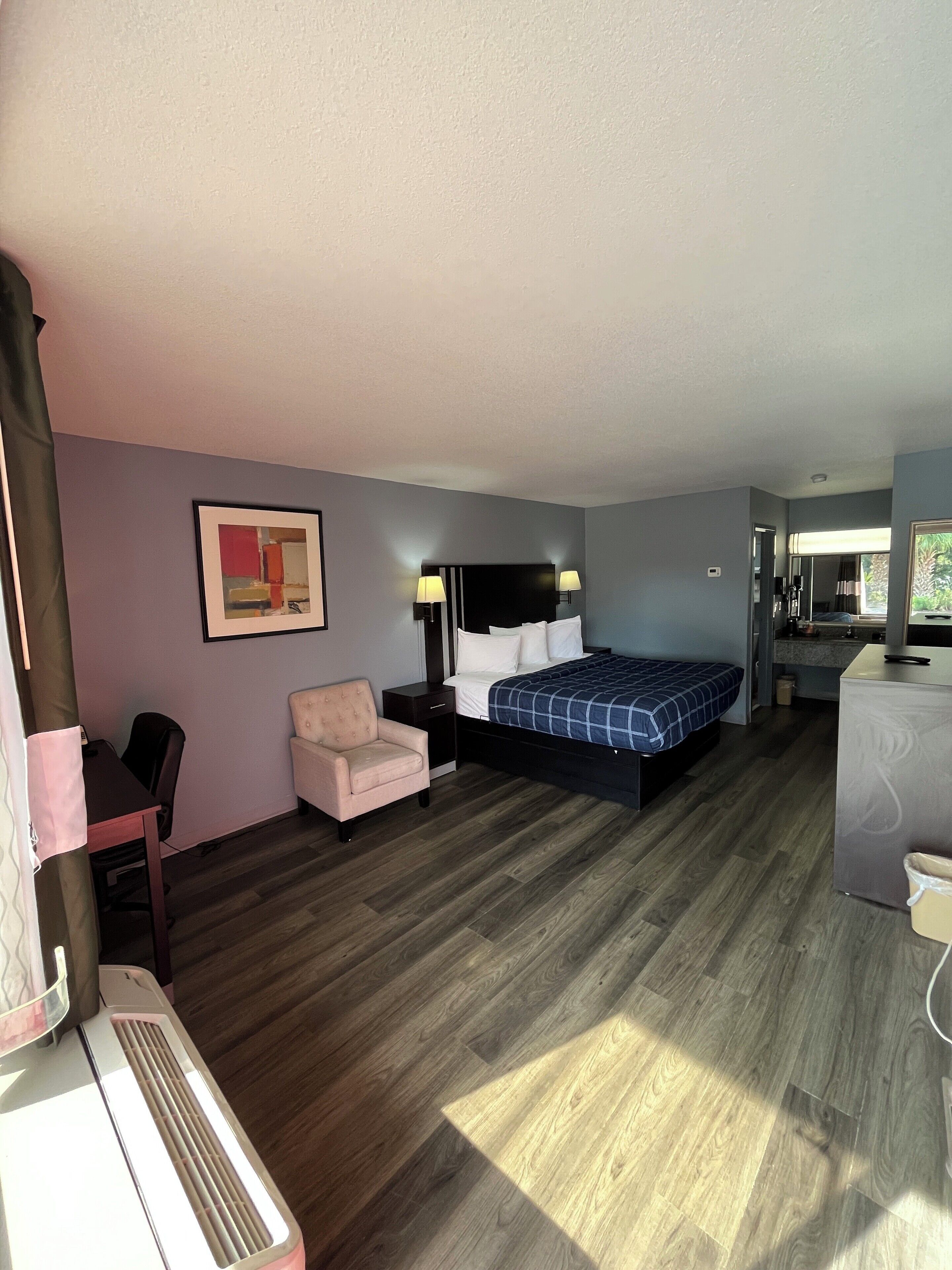 A compact hotel room with a bed, a desk, a chair, and a small kitchenette.