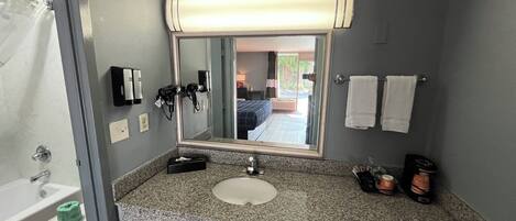 A bathroom with a sink, mirror, towel rack, and a view of a bedroom with a bed and window.
