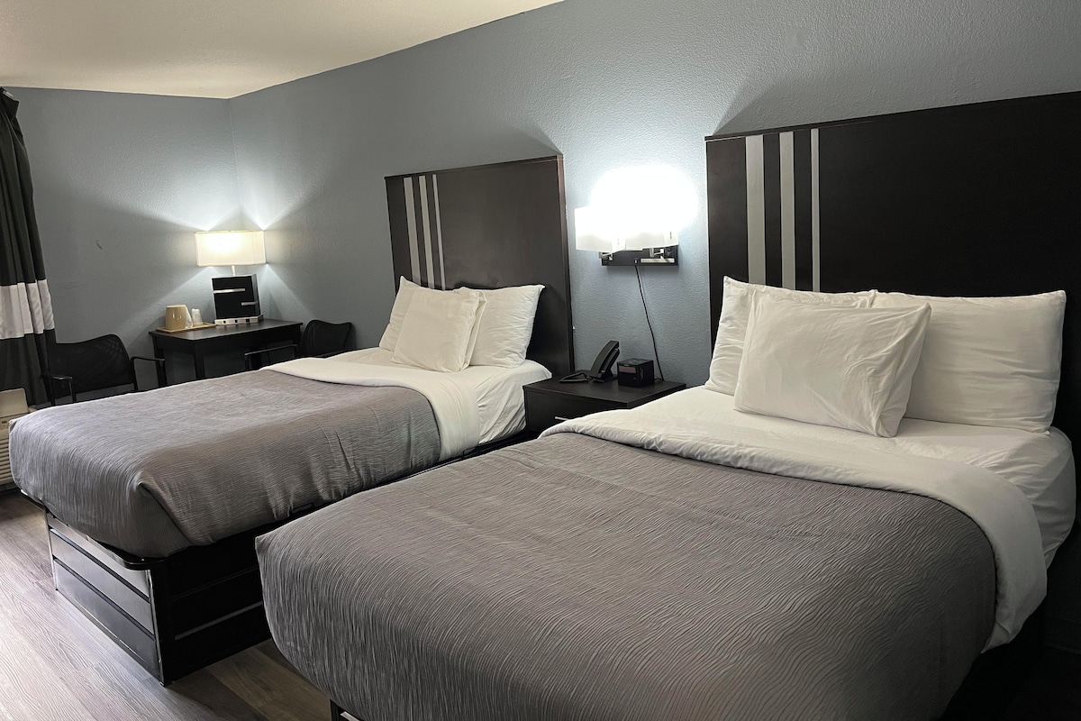 A hotel room with two beds, a desk, a chair, a lamp, and a nightstand.