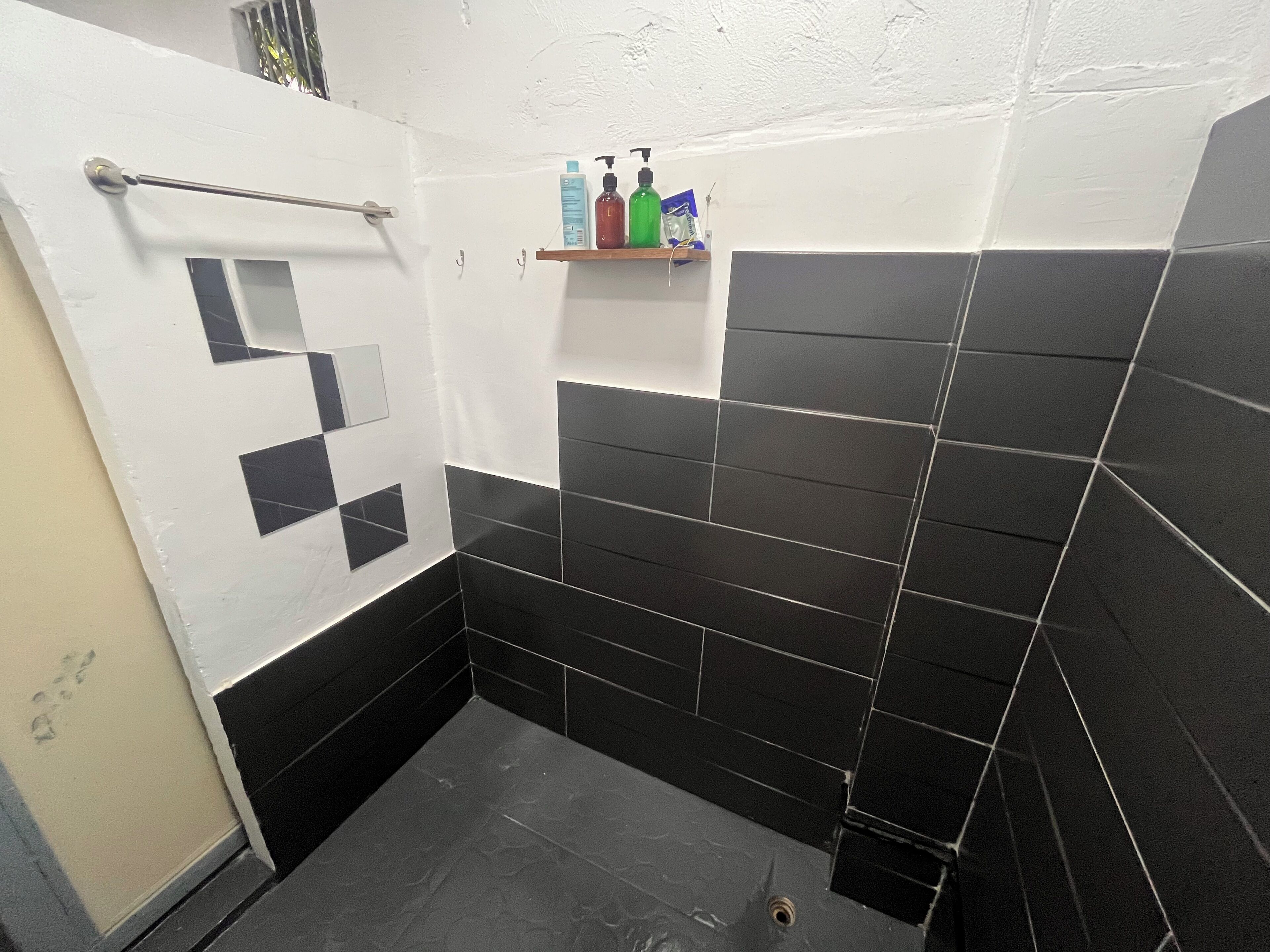 Un baño con baldosas blanco y negro, zona de ducha y un estante con artículos de aseo.