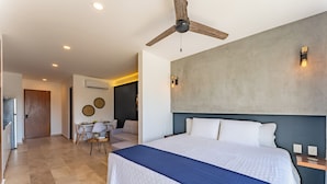 Et hotelværelse med en stor seng, en loftsvift, et spiseområde med bord og stole, samt et moderne vægdesign.