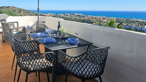 An outdoor dining area with a table set for two, a wine bottle, and a potted plant. - Seaview apartment in El Porton Calahonda (Sitio de Calahonda)