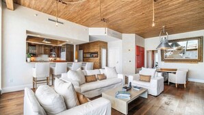 A spacious living area with a high ceiling and exposed wooden beams, a kitchen in the background, and a large mirror on the wall. - Stunning Oceanfront Penthouse at the Ritz-Carlton on Singer Island (Riviera Beach)