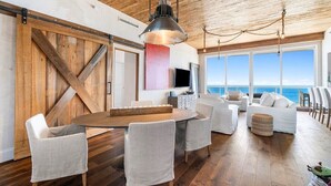 A spacious dining area with a wooden table and chairs, a large sliding barn door, and a view of the ocean. - Stunning Oceanfront Penthouse at the Ritz-Carlton on Singer Island (Riviera Beach)
