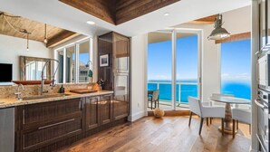 A modern kitchen with dark wood cabinets, a large island, and a view of the ocean through a sliding glass door. - Stunning Oceanfront Penthouse at the Ritz-Carlton on Singer Island (Riviera Beach)