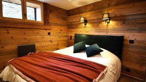 A wooden-paneled bedroom with a bed, two wall-mounted lamps, and a window.