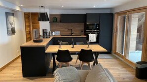 A modern kitchen with a central island, black chairs, a dining table, and a sofa in a living area.