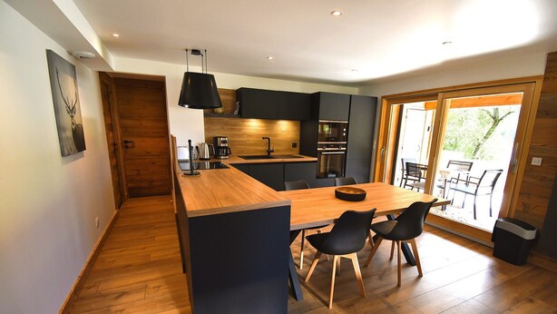 A modern kitchen with a wooden island, black chairs, and a dining table.