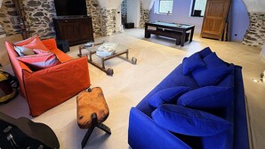 Amplia sala de estar con pared de piedra, mesa de billar y televisor.
