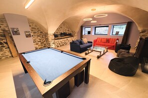 Ein Billardtisch in einem Raum mit Steinwänden, einem roten Sofa und einem Glastisch.