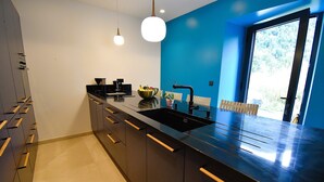 Cocina moderna con encimeras y pileta negros, y una pared de acento azul. Hay armarios de madera con herrajes y un lámpara colgante.