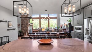 A spacious kitchen with a large wooden table, modern appliances, and a stone fireplace. - Spacious 5-bedroom house in Montreat with stunning views, spa, fitness room (Black Mountain)