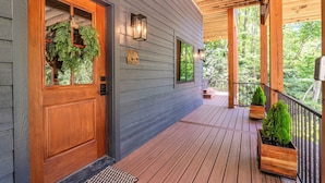 A wooden deck with a wooden door and windows, a covered porch, and potted plants. - Spacious 5-bedroom house in Montreat with stunning views, spa, fitness room (Black Mountain)