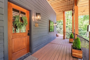 Une terrasse en bois avec une porte et des fenêtres en bois, un porche couvert et des plantes en pot.