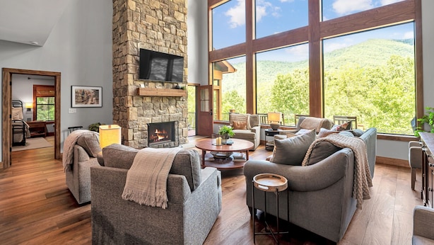A spacious living room with a stone fireplace, large windows offering a mountain view, and modern furniture. - Spacious 5-bedroom house in Montreat with stunning views, spa, fitness room (Black Mountain)