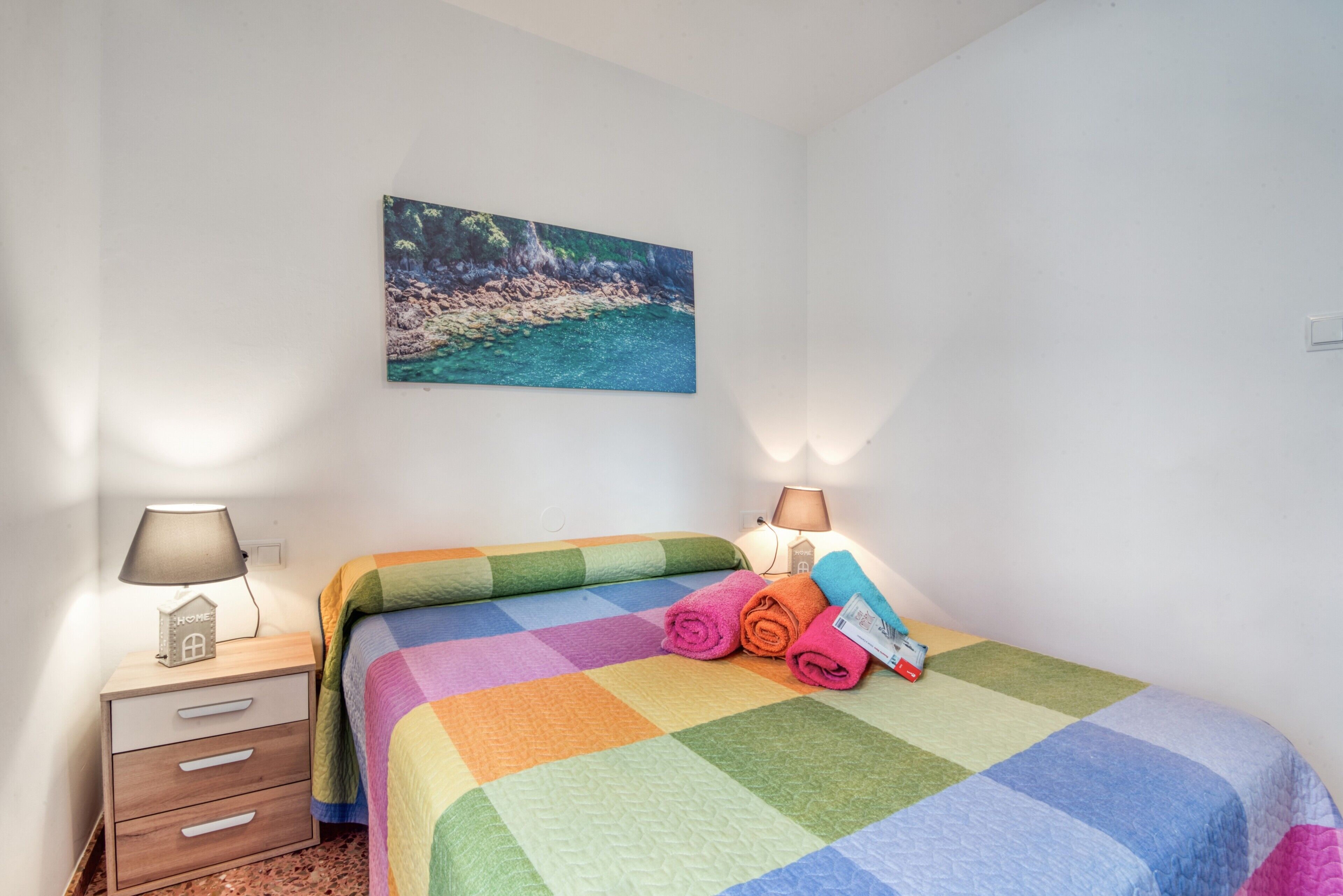A bedroom with a bed, a nightstand, a lamp, and a painting on the wall.
