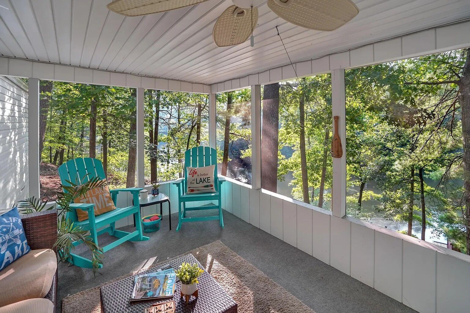 A covered porch with two turquoise Adirondack chairs, a small table, and a wicker chair.