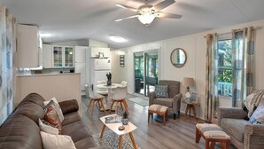 Un salon moderne avec un canapé en cuir marron, une table basse ronde et un coin repas comprenant une table et des chaises blanches.