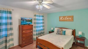 Une chambre avec un lit en bois, une commode, un téléviseur et un panneau indiquant « Détendez-vous ».