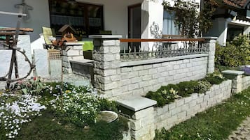 Un mur de pierre surmonté d’une rambarde métallique, un vélo et un petit jardin fleuri.