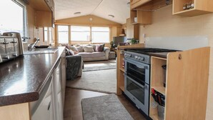 A compact RV kitchen with a stove, oven, and toaster. There is a sofa and a dining table in the living area. - Caravan 596 (Prestatyn)