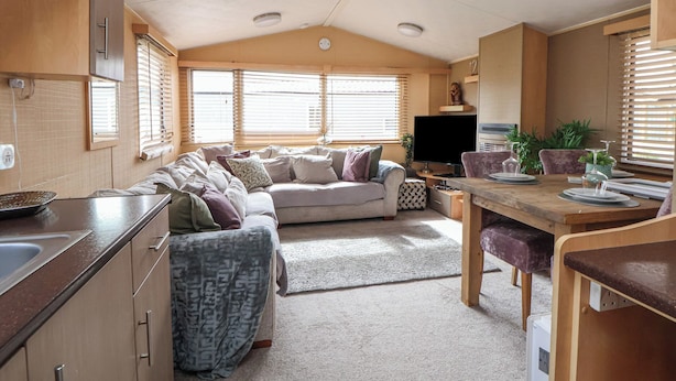 A compact RV interior with a kitchenette, a sofa, a dining table, and a TV. - Caravan 596 (Prestatyn)