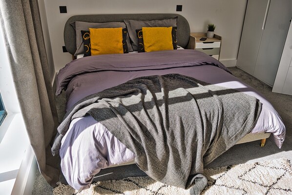 A bedroom with a bed, a nightstand, a wardrobe, and a window with curtains.