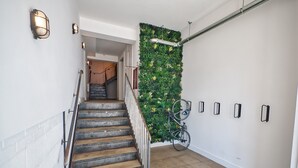 Eine Treppe mit Metallgeländer, eine grüne Wand mit Pflanzen und ein an der Wand befestigtes Fahrrad.