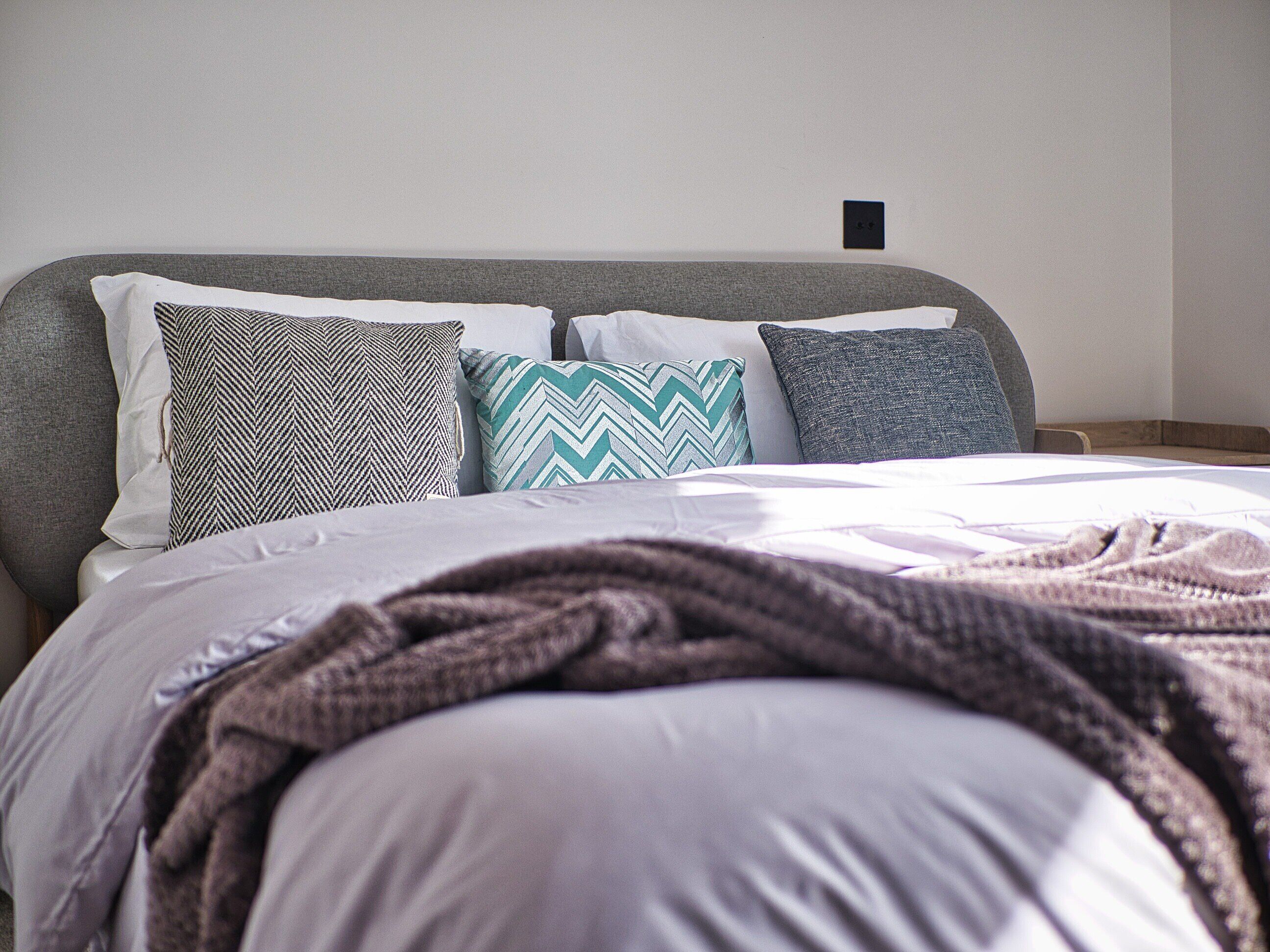 A neatly made bed with a grey headboard, multiple pillows, and a blanket.