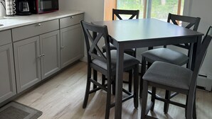 Moderni keittiö, jossa on ruokapöytä ja -tuolit, mikroaaltouuni ja kahvinkeitin.