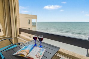 Un balcón con una mesa, dos copas de vino y una revista abierta.
