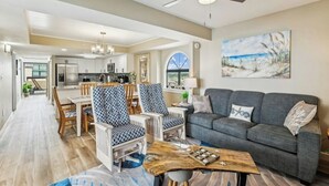 A modern living room with a gray sofa, patterned chairs, a wooden coffee table, and a painting of a beach scene.