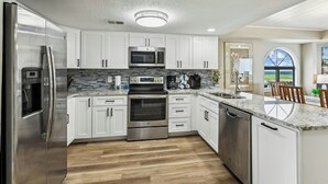 A modern kitchen with stainless steel appliances, white cabinetry, and a wooden floor.
